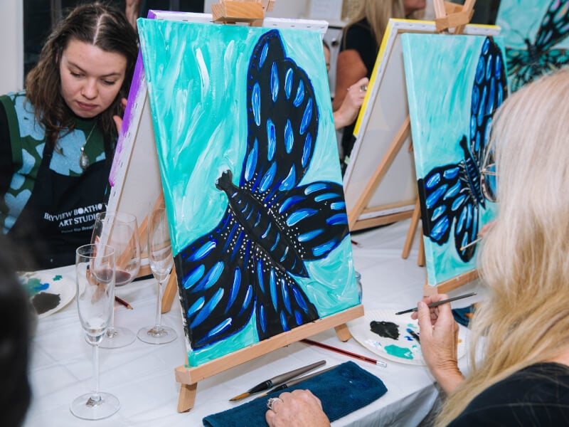 Woman painting a butterfly at a brush and sip class